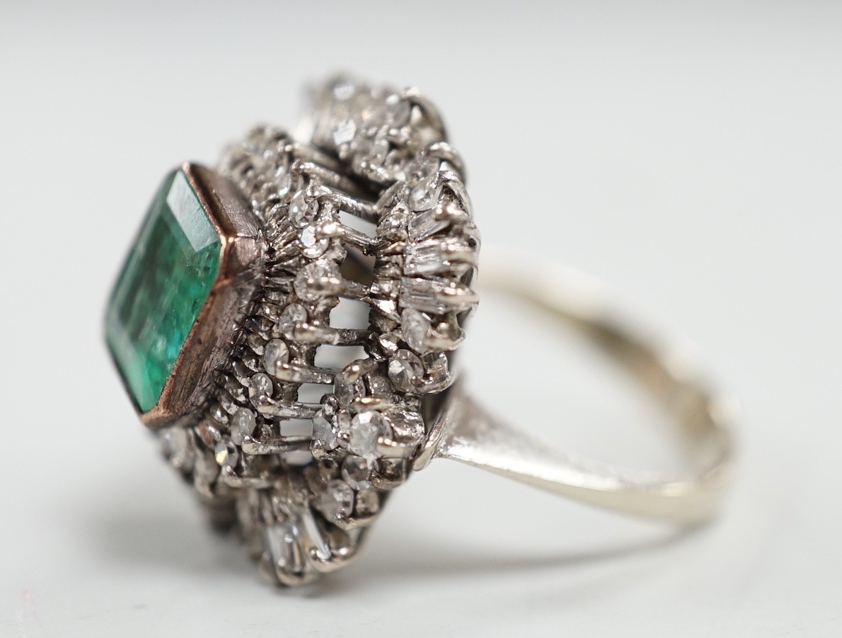 A white metal and single stone emerald set dress ring, bordered with two stepped bands of round and baguette cut diamonds, size K, gross weight 7.6 grams.